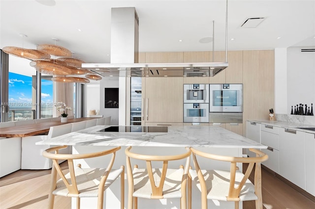 kitchen featuring a breakfast bar, stainless steel double oven, modern cabinets, and light stone counters