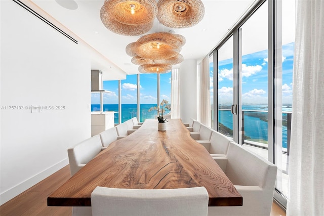 dining room featuring a water view, baseboards, floor to ceiling windows, and wood finished floors