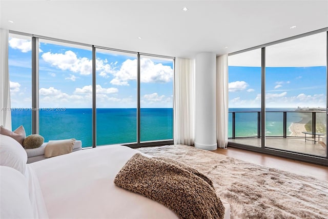 bedroom featuring a water view, access to exterior, floor to ceiling windows, and wood finished floors