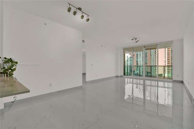 spare room with marble finish floor, a wall of windows, and baseboards