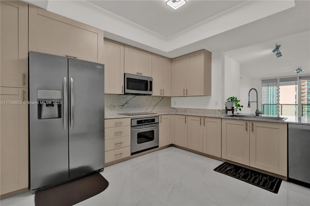 kitchen with stainless steel appliances, a sink, marble finish floor, cream cabinetry, and decorative backsplash