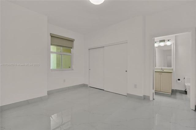 unfurnished bedroom with a sink, baseboards, marble finish floor, a closet, and ensuite bath