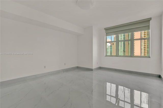 spare room featuring marble finish floor and baseboards