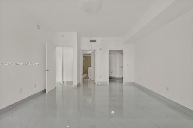 unfurnished bedroom with a walk in closet, marble finish floor, visible vents, and baseboards