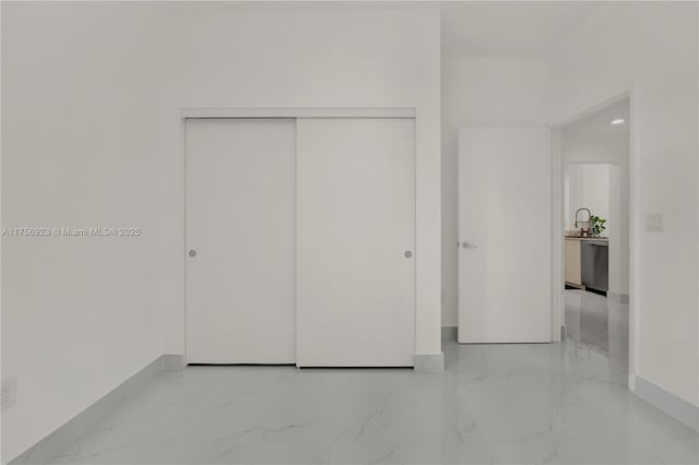 unfurnished bedroom with a closet, marble finish floor, a sink, and baseboards