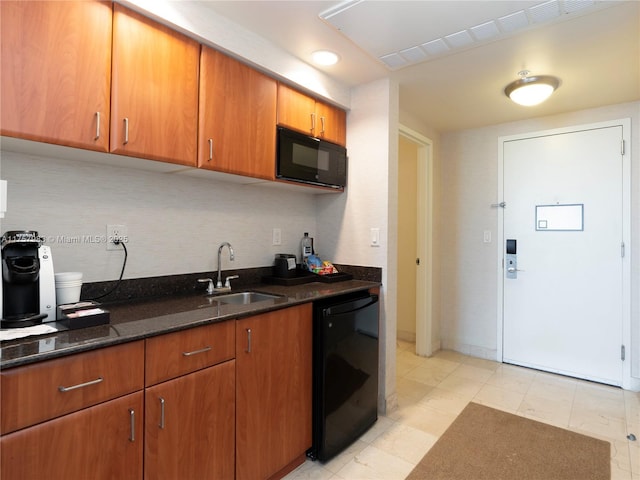 kitchen featuring brown cabinetry, dark stone counters, a sink, and black appliances