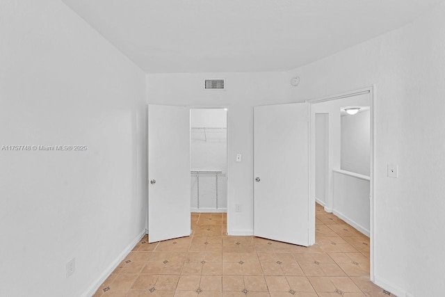 unfurnished bedroom with light tile patterned floors, visible vents, baseboards, a closet, and a walk in closet