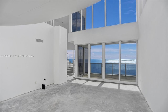 empty room featuring a towering ceiling, a water view, visible vents, and concrete flooring