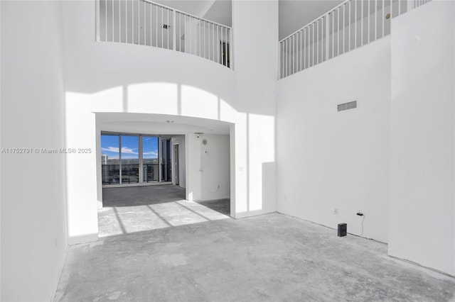 unfurnished living room featuring concrete flooring, visible vents, and a high ceiling