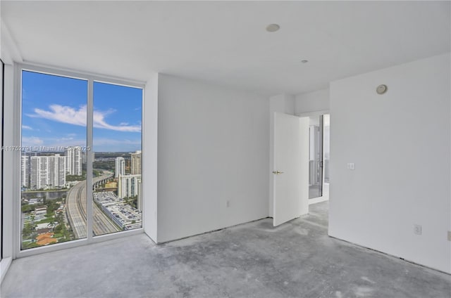 spare room featuring expansive windows, a city view, and unfinished concrete floors