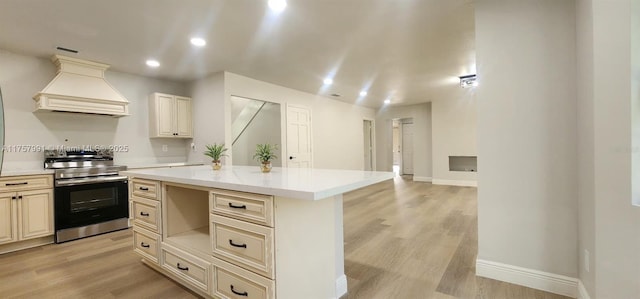 kitchen with light wood finished floors, electric stove, custom range hood, cream cabinets, and light countertops