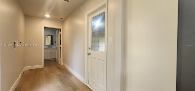 hall featuring baseboards, a sink, and light wood-style floors