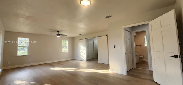 unfurnished bedroom with baseboards, a barn door, visible vents, and wood finished floors