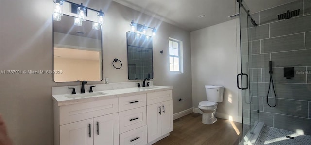 full bathroom with double vanity, a stall shower, toilet, wood finished floors, and a sink