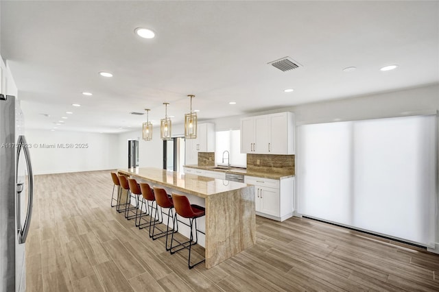 kitchen featuring visible vents, light stone counters, stainless steel appliances, a kitchen bar, and a sink