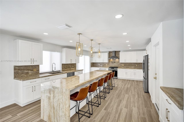 kitchen with a center island, a breakfast bar area, stainless steel appliances, a sink, and wall chimney range hood