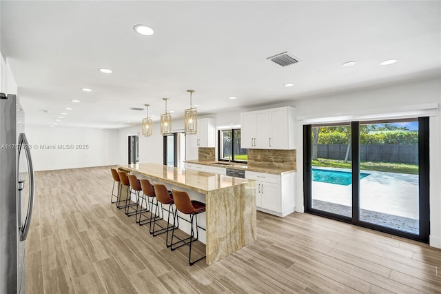 kitchen with visible vents, a breakfast bar, freestanding refrigerator, light stone countertops, and backsplash