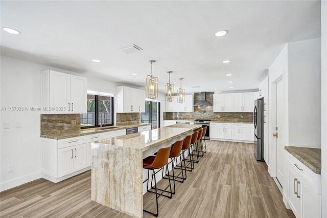 kitchen featuring stainless steel appliances, a kitchen island, wall chimney range hood, light stone countertops, and a kitchen bar