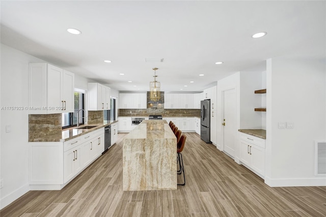 kitchen featuring stainless steel appliances, decorative backsplash, a sink, light stone countertops, and light wood-type flooring