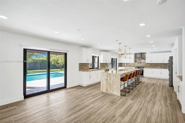 kitchen with appliances with stainless steel finishes, a breakfast bar, a center island, wall chimney range hood, and a sink