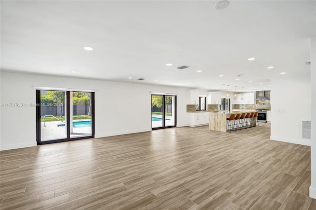 unfurnished living room featuring baseboards, light wood finished floors, visible vents, and recessed lighting