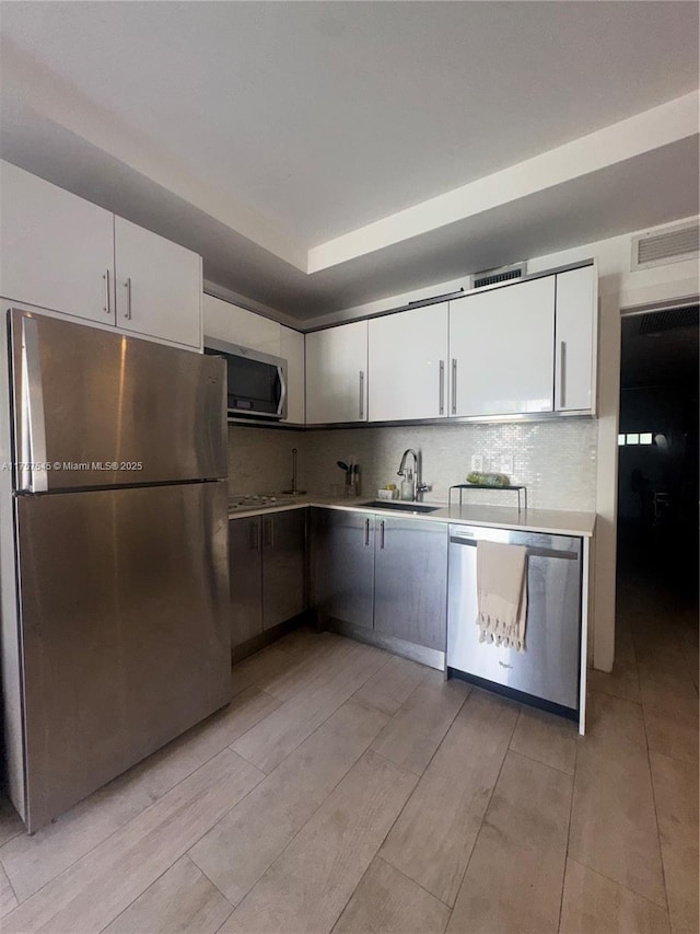 kitchen with tasteful backsplash, light countertops, white cabinetry, appliances with stainless steel finishes, and a sink
