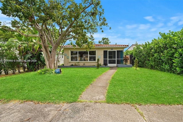 view of front of property featuring a sunroom, a tiled roof, a front lawn, and stucco siding