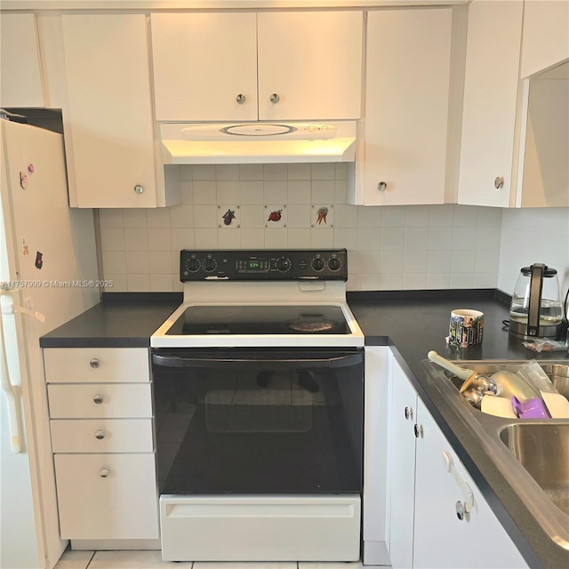 kitchen featuring under cabinet range hood, electric stove, freestanding refrigerator, tasteful backsplash, and dark countertops