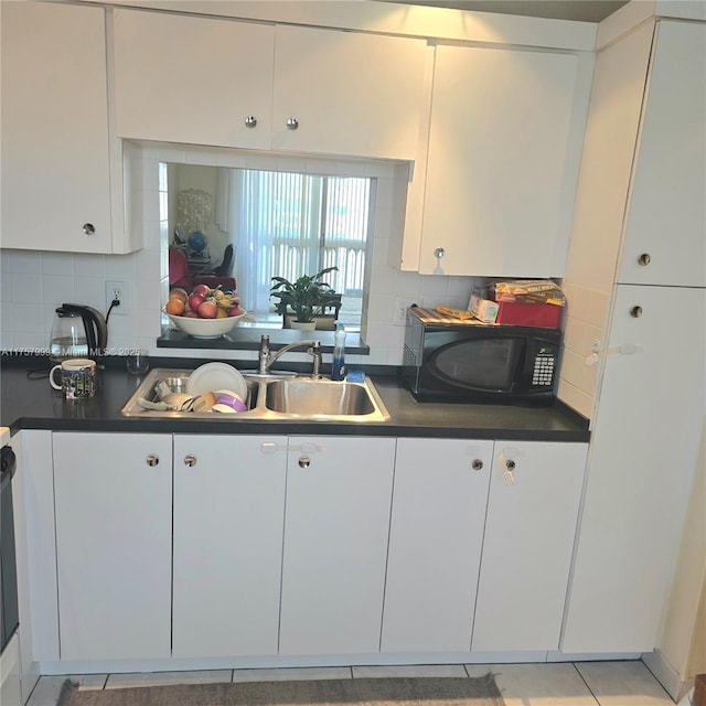 kitchen with black microwave, a sink, white cabinets, backsplash, and dark countertops