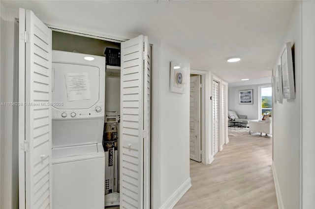 washroom with stacked washer and dryer, laundry area, light wood-style floors, and baseboards