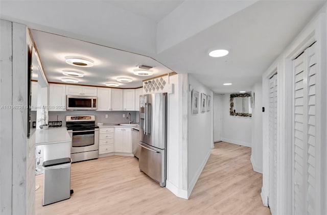 kitchen with light wood finished floors, light countertops, appliances with stainless steel finishes, and white cabinets