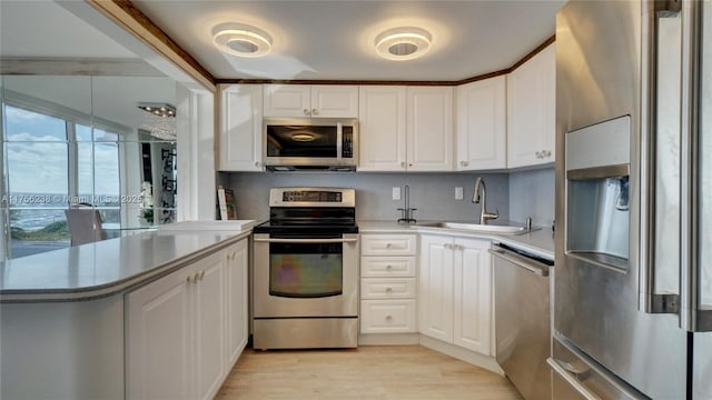 kitchen featuring stainless steel appliances, a peninsula, a sink, white cabinets, and light wood-type flooring