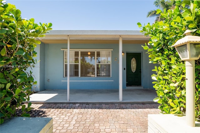 view of exterior entry with a porch and stucco siding