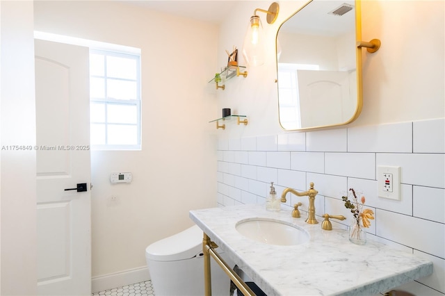 bathroom featuring tile walls, visible vents, toilet, vanity, and baseboards