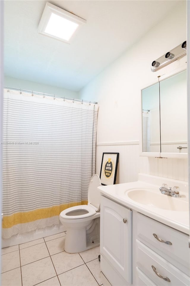 bathroom with a wainscoted wall, a shower with shower curtain, toilet, vanity, and tile patterned flooring