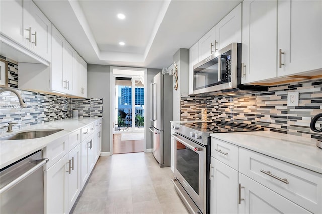 kitchen featuring a raised ceiling, light countertops, appliances with stainless steel finishes, white cabinets, and a sink