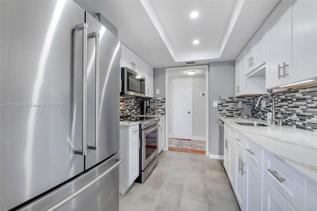 kitchen with a sink, white cabinets, appliances with stainless steel finishes, backsplash, and a tray ceiling