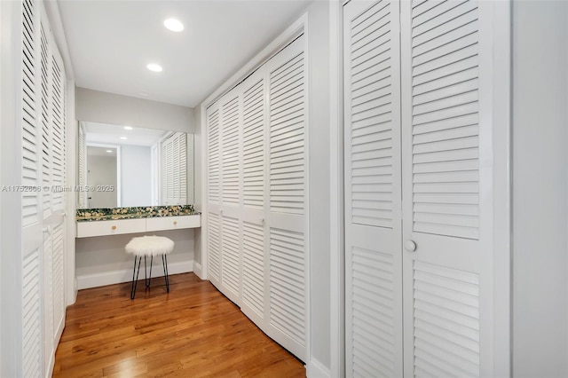 hall featuring baseboards, light wood-type flooring, and recessed lighting