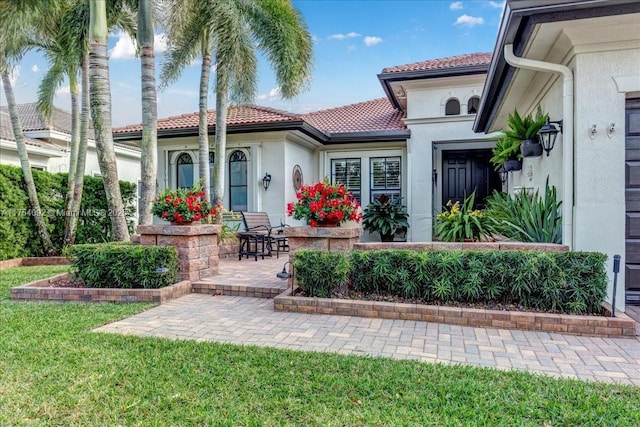 view of exterior entry with a yard, a tiled roof, and stucco siding