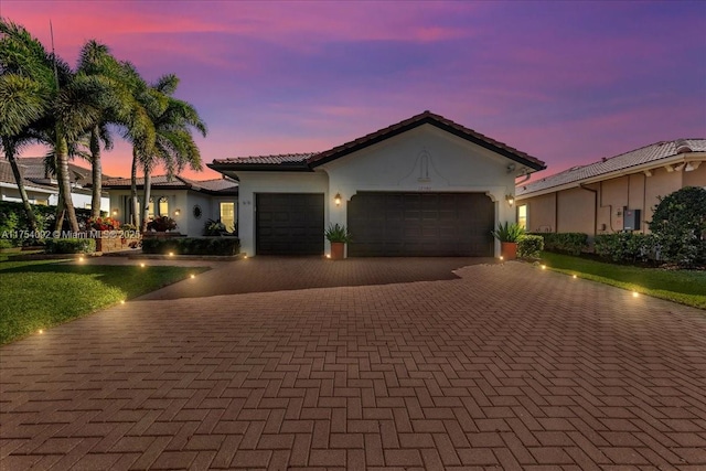 view of front of house with decorative driveway, a tiled roof, an attached garage, and stucco siding