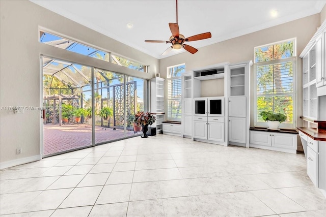 unfurnished living room with light tile patterned floors, ceiling fan, a sunroom, baseboards, and crown molding