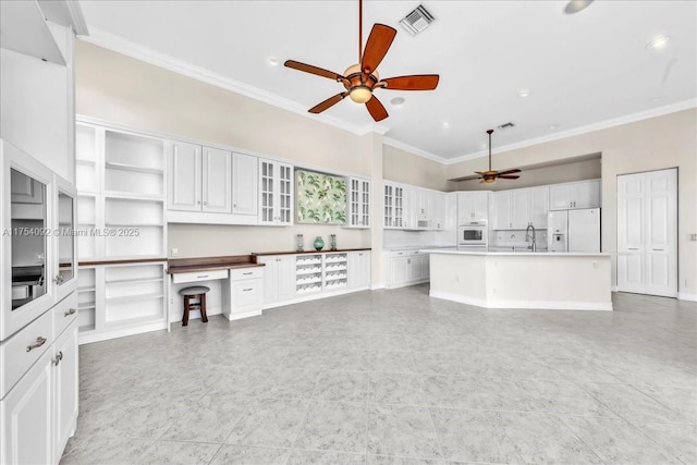 kitchen with white appliances, visible vents, built in desk, and ornamental molding