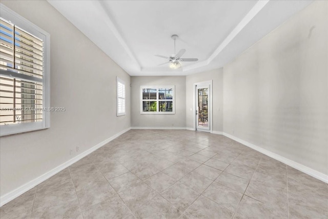 tiled empty room with baseboards, a raised ceiling, and a ceiling fan