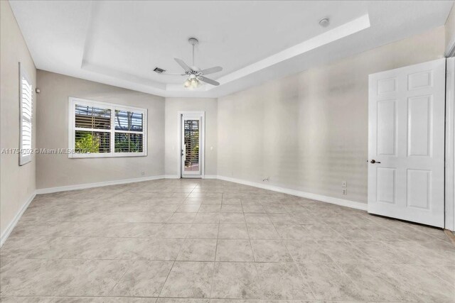 spare room featuring a ceiling fan, a raised ceiling, visible vents, and baseboards