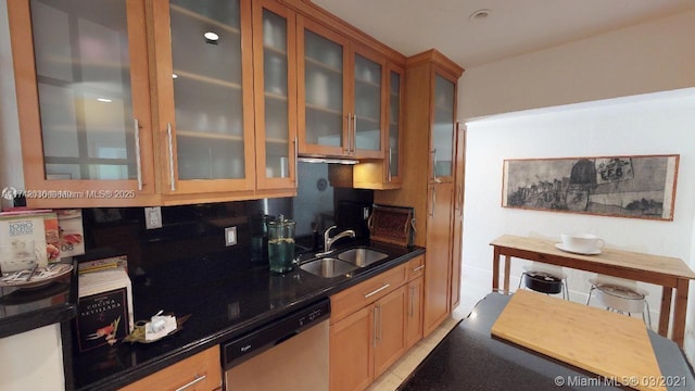 kitchen with glass insert cabinets, dark stone countertops, dishwasher, and a sink