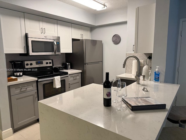 kitchen with light stone counters, light tile patterned flooring, a peninsula, appliances with stainless steel finishes, and decorative backsplash