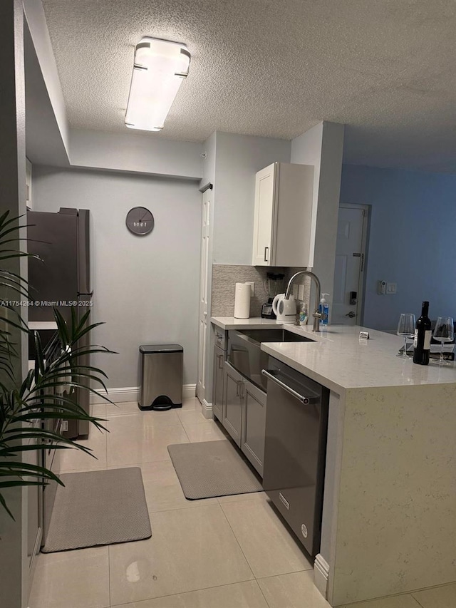 kitchen with light tile patterned floors, tasteful backsplash, a sink, a textured ceiling, and dishwasher