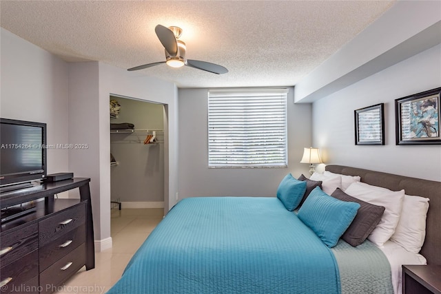 bedroom featuring a walk in closet, light tile patterned floors, a closet, ceiling fan, and a textured ceiling