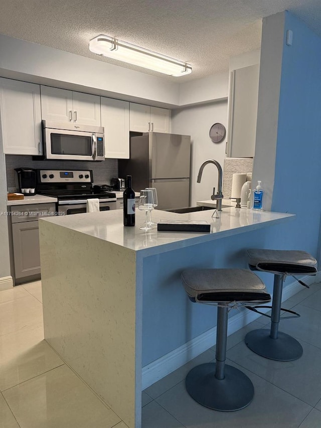 kitchen featuring appliances with stainless steel finishes, light tile patterned flooring, a textured ceiling, a peninsula, and a kitchen bar