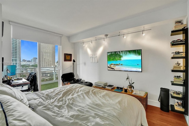 bedroom with access to outside, wood finished floors, and track lighting